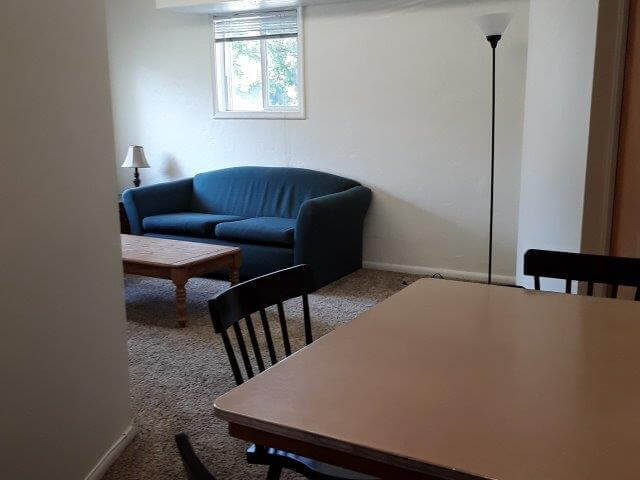 Dining table and chairs; looking beyond into the living room with sofa, coffee table, and torchiere lamp.