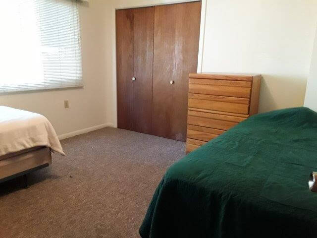 Shared-bedroom showing two twin beds, 5-drawer dresser (second dresser not shown), closet and large window.